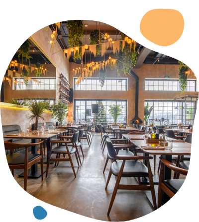 Modern, stylish restaurant interior with wooden tables, black chairs, large windows, and hanging greenery from the ceiling.